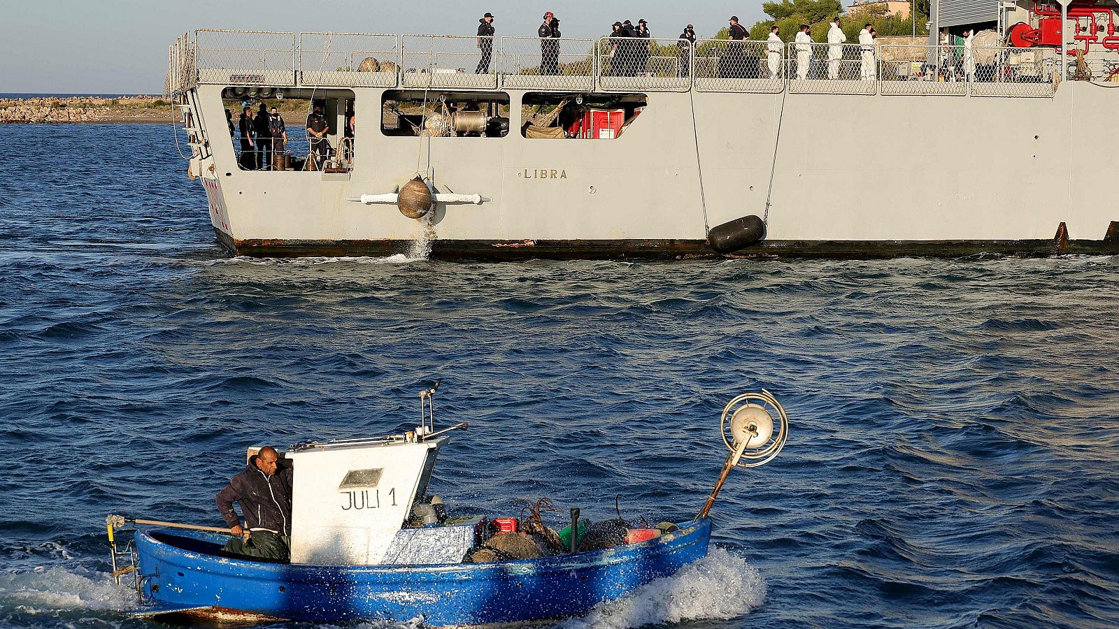 Un barco pesquero pasa junto a un barco de la marina que transportaba migrantes interceptados en aguas italianas y llega a Albania. El barco italiano con el primer grupo de migrantes trasladados a Albania llega al país.