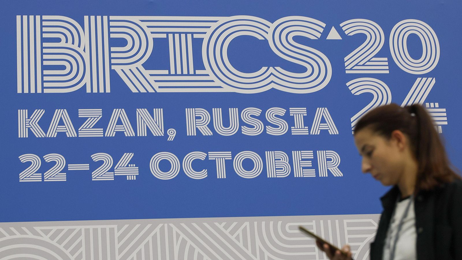 Una mujer revisa su teléfono en el edificio Kazan Expo, el lugar principal de la cumbre BRICS 2024 en Kazán. Putin recibe en Rusia a los líderes de los BRICS mientras sus tropas siguen avanzando en Ucrania.