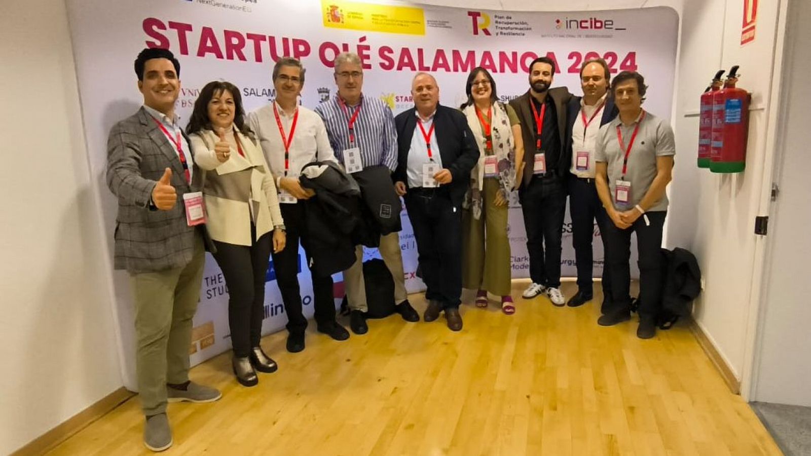 En la imagen aparecen reunidos el equipo de Impulsa Visión RTVE y responsables de Cátedras RTVE sonriendo a cámara y posando frente a un photocall de Startup Olé 2024