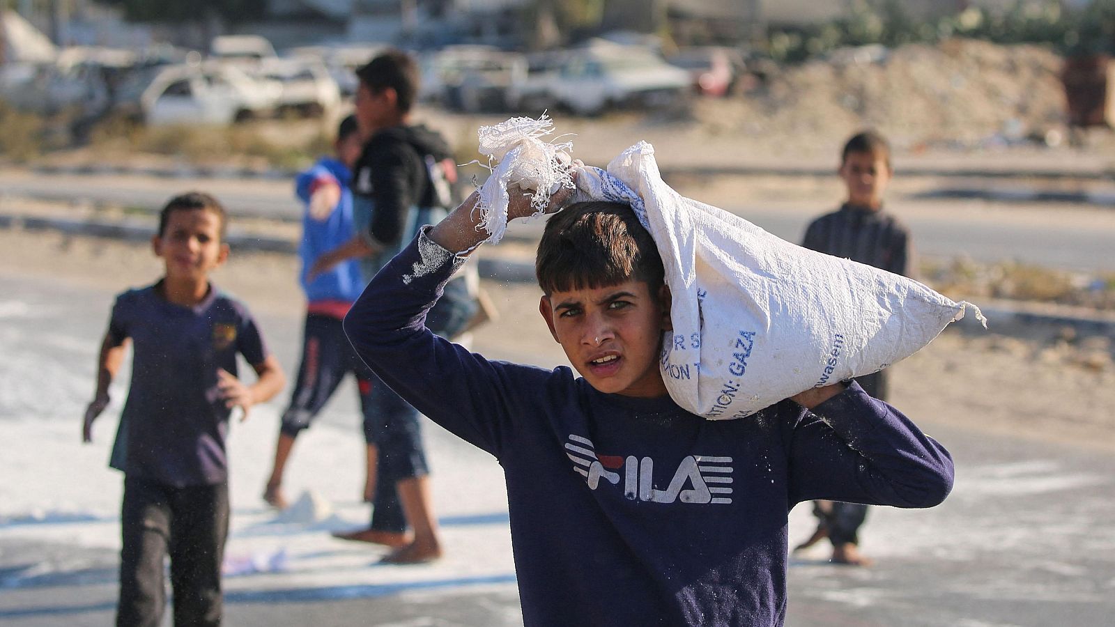 Niños palestinos recogen harina del suelo de una bolsa que cayó de un camión de ayuda que circulaba por una carretera en la Franja de Gaza. Los ataques aéreos israelíes matan al menos a 30 palestinos en Gaza en las últimas 24 horas.