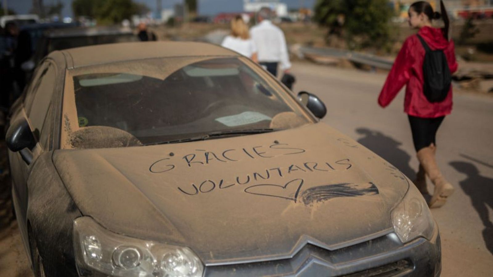 Un coche cubierto de barro tiene escrito en su capó "Gracies voluntaris".