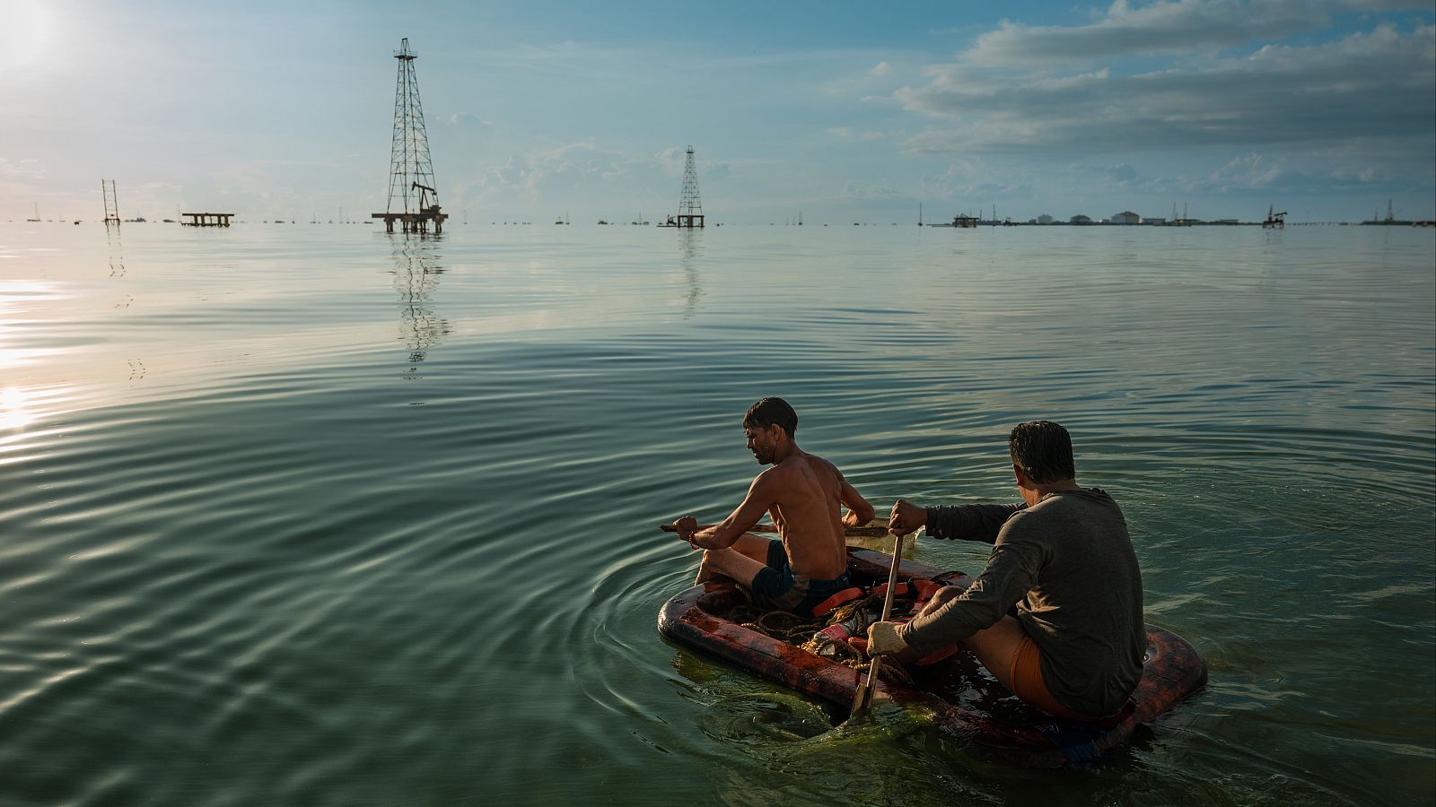 Dos pescadors remen per les aigües verdes del llac Maracaibo, que, a més de petroli, està cobert per algues nocives que proliferen per culpa del vessament de fertilitzants, aigües residuals i altres productes químics. Cabimas, Veneçuela, 24 de novembre de 2022.