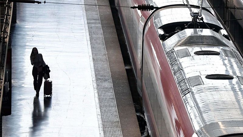 Viajera con maleta camina por el andén junto a un AVE de Renfe, tras la reanudación del servicio Madrid-Valencia.