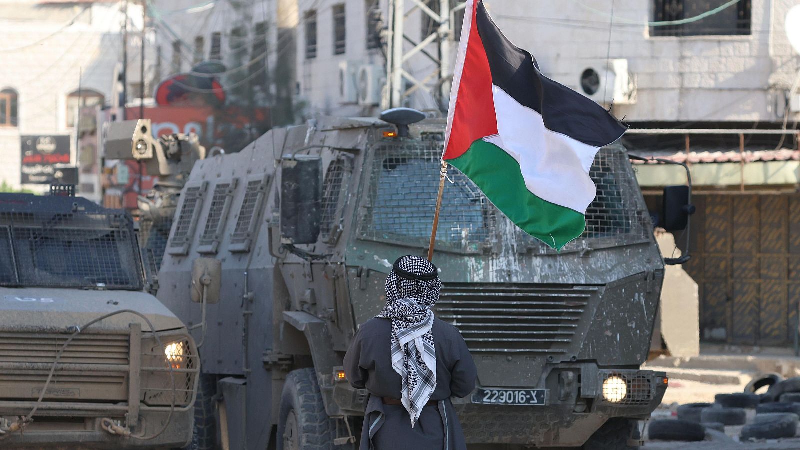 Un hombre ondea una bandera palestina junto a vehículos militares y excavadoras israelíes durante una redada llevada a cabo por las fuerzas israelíes en la ciudad cisjordana de Tulkarem