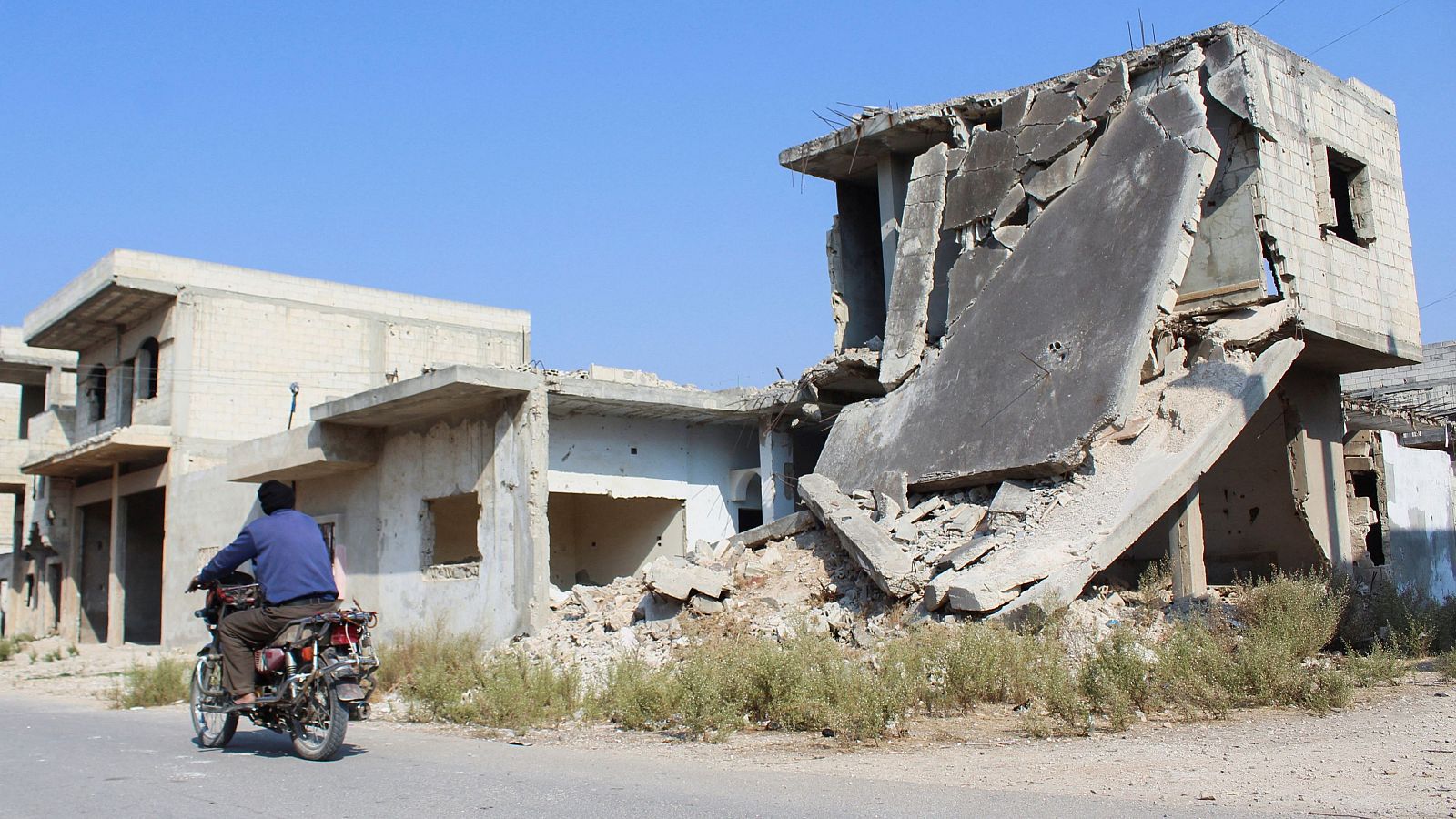 Un hombre pasa en moto junto a un edificio destruido en Homs, Siria