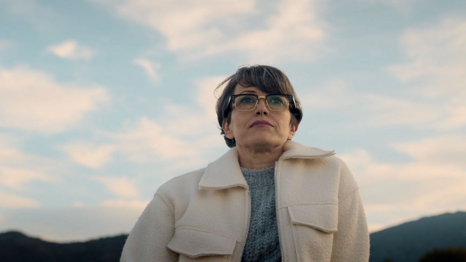 La periodista Gemma Nierga posa seria con una chaqueta blanca y gafas, mirando al horizonte en un día nublado.