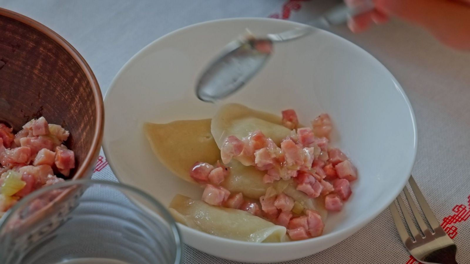 Empanadillas ucranianas (Varenyky) con bacon en un bol blanco, una cuchara a punto de servirlas.