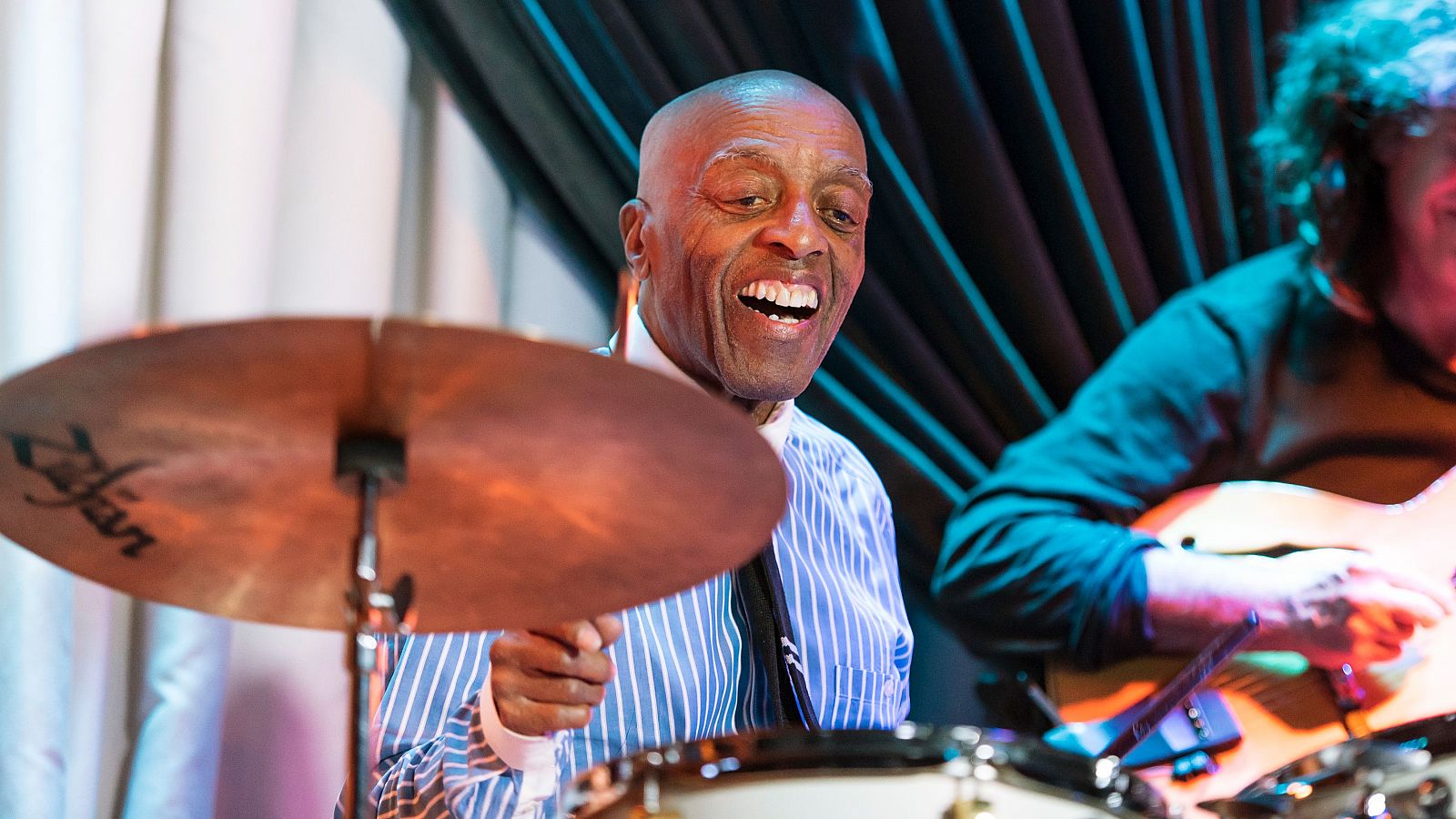 Roy Haynes, baterista de jazz, toca con entusiasmo en un concierto, mostrando una gran sonrisa.