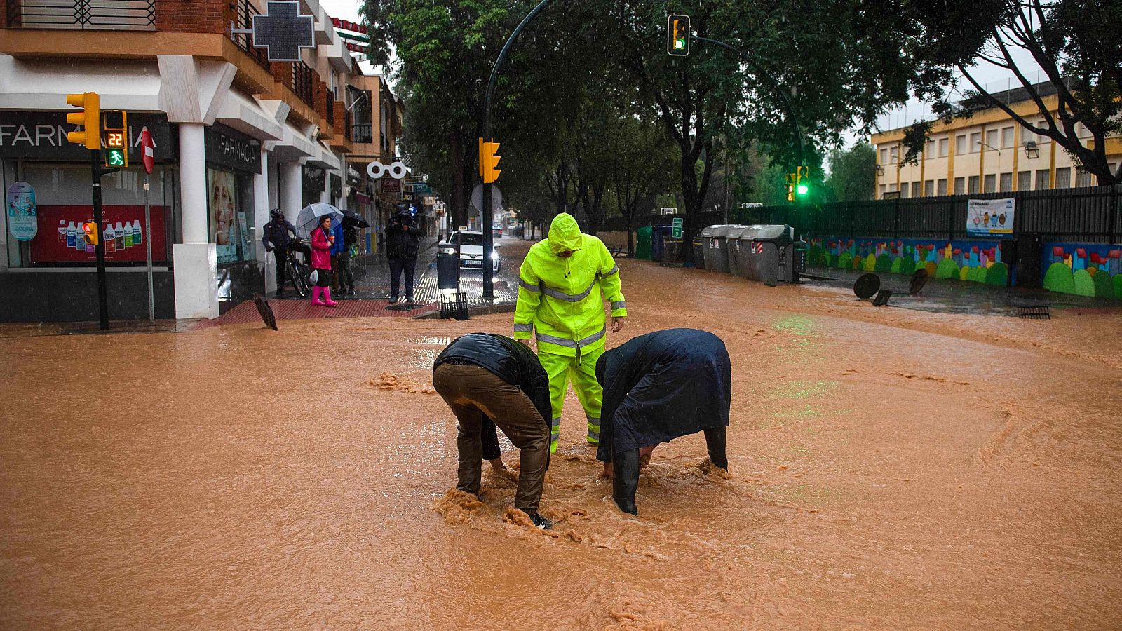 Varios trabajadores desatascan una alcantarilla mientras una calle se inunda en Campanillas, Málaga