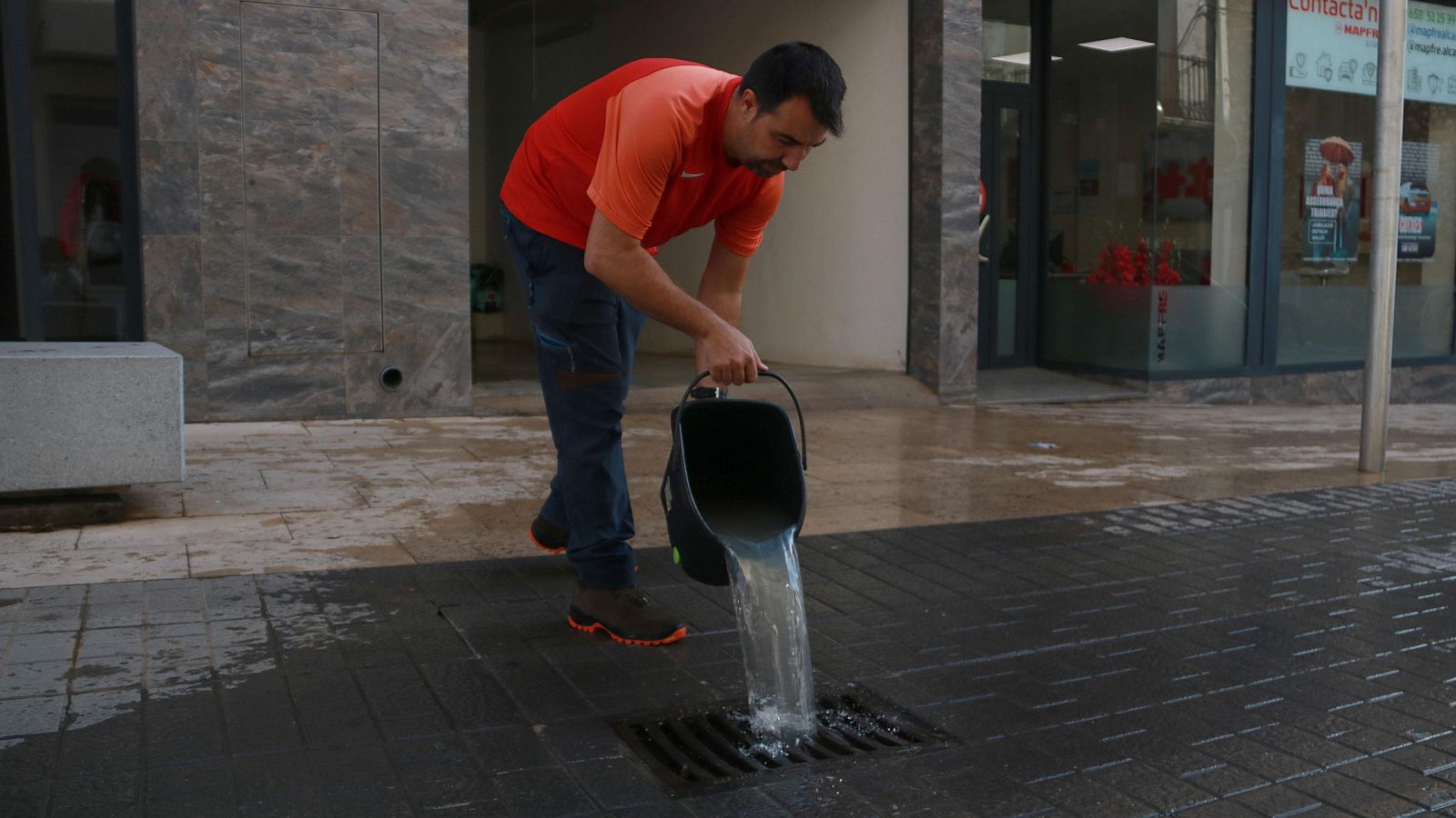 Un hombre vacía un cubo de agua en una alcantarilla en Joaquín, veí d'Alcanar, tras las fuertes lluvias que han afectado a la localidad.