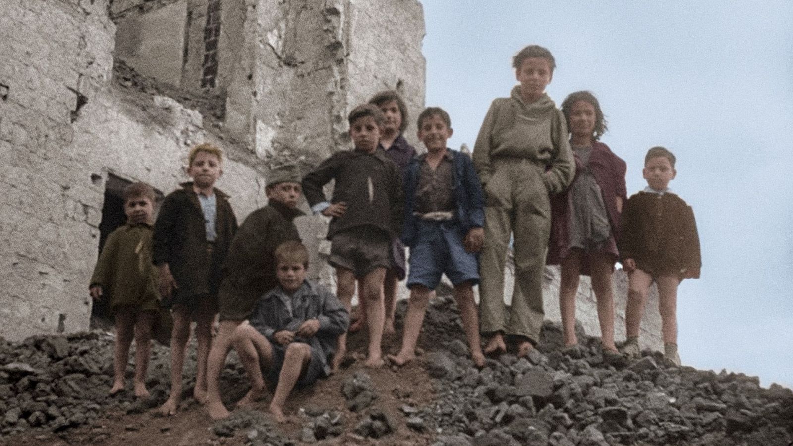 Grupo de niños descalzos frente a un edificio en ruinas, en una imagen coloreada que refleja la dureza de la posguerra.