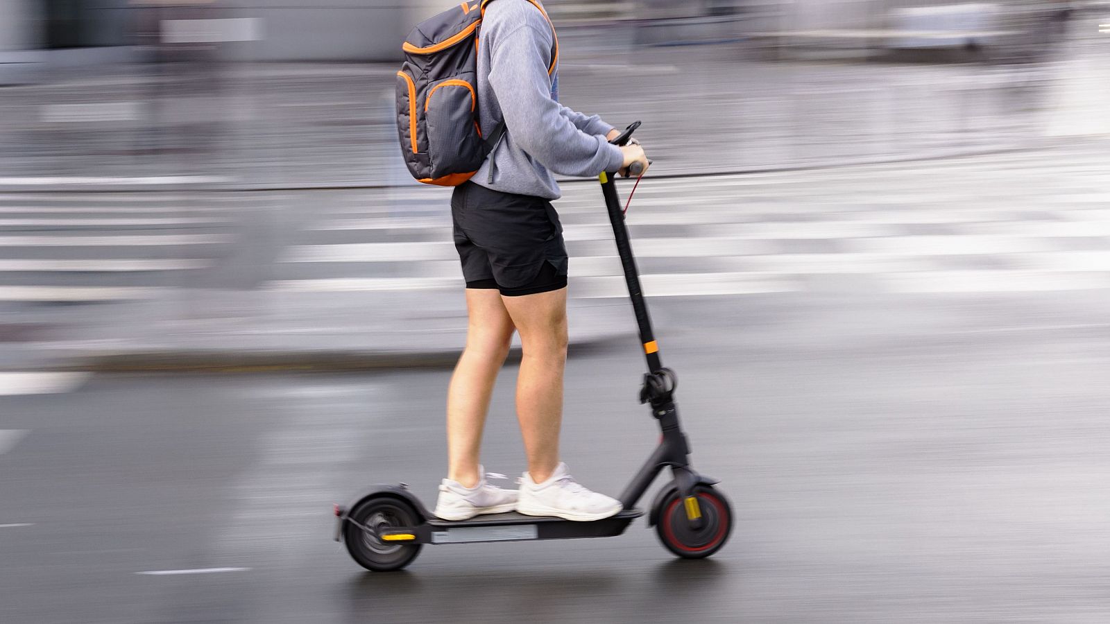 Persona con mochila conduciendo un patinete eléctrico por la carretera a velocidad.