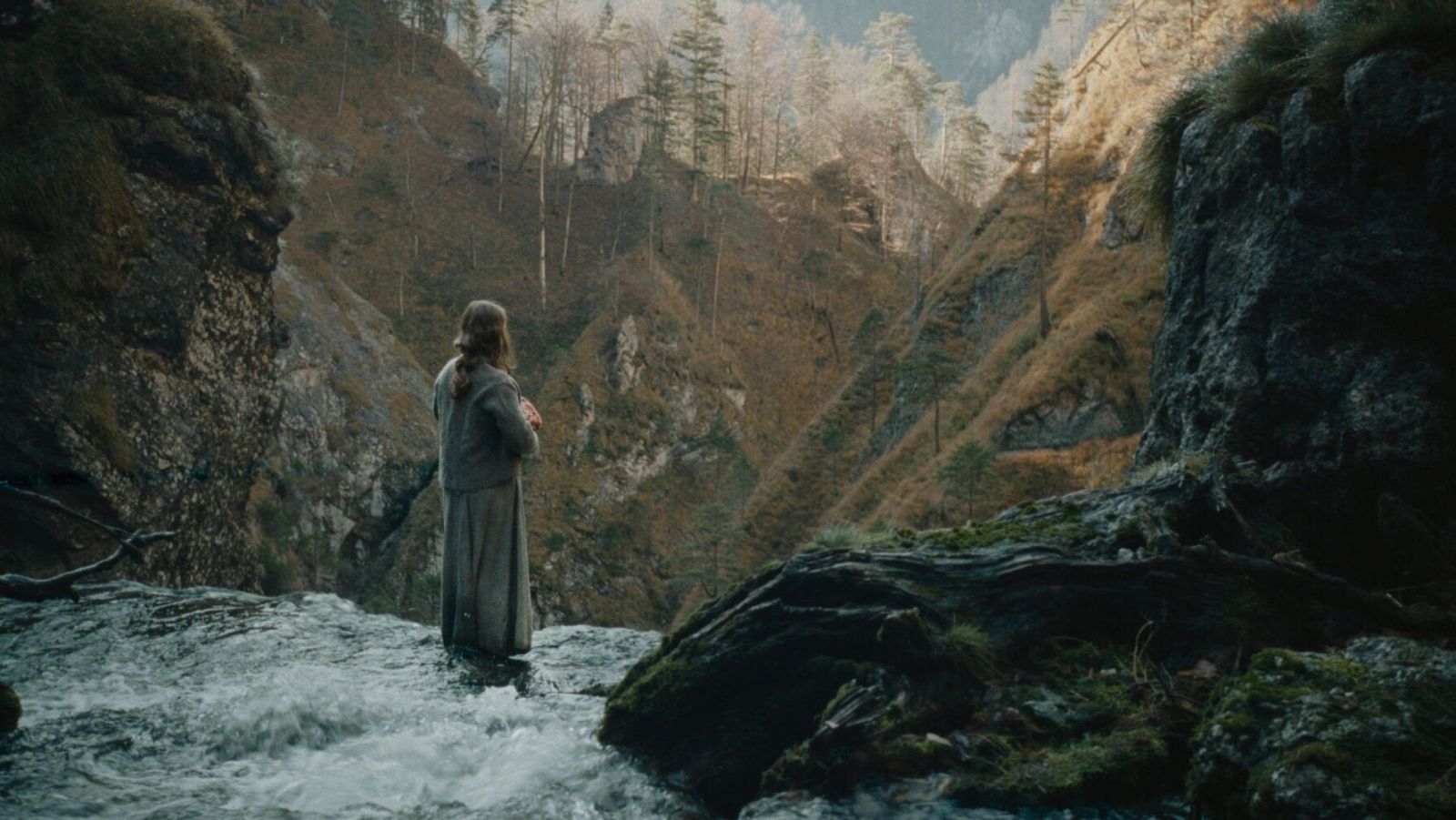 Mujer de espaldas contempla un valle desde lo alto de una cascada.