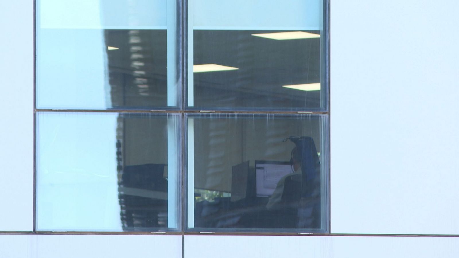 Una persona trabaja en su ordenador en una oficina vista desde fuera del edificio.