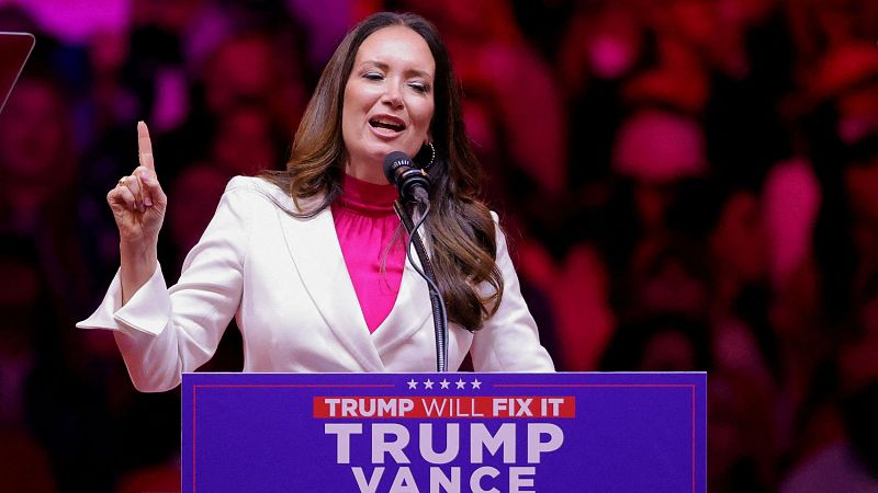 Brooke L. Rollins da un discurso en un atril con el lema "TRUMP WILL FIX IT" y "TRUMP VANCE". Lleva un traje blanco y blusa rosa.