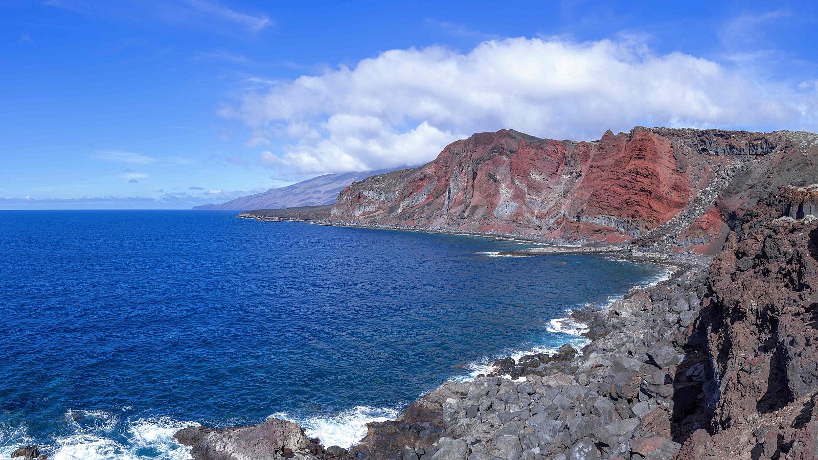 El Mar de las Calmas en El Hierro, con cielo azul, acantilados rojizos y costa rocosa.