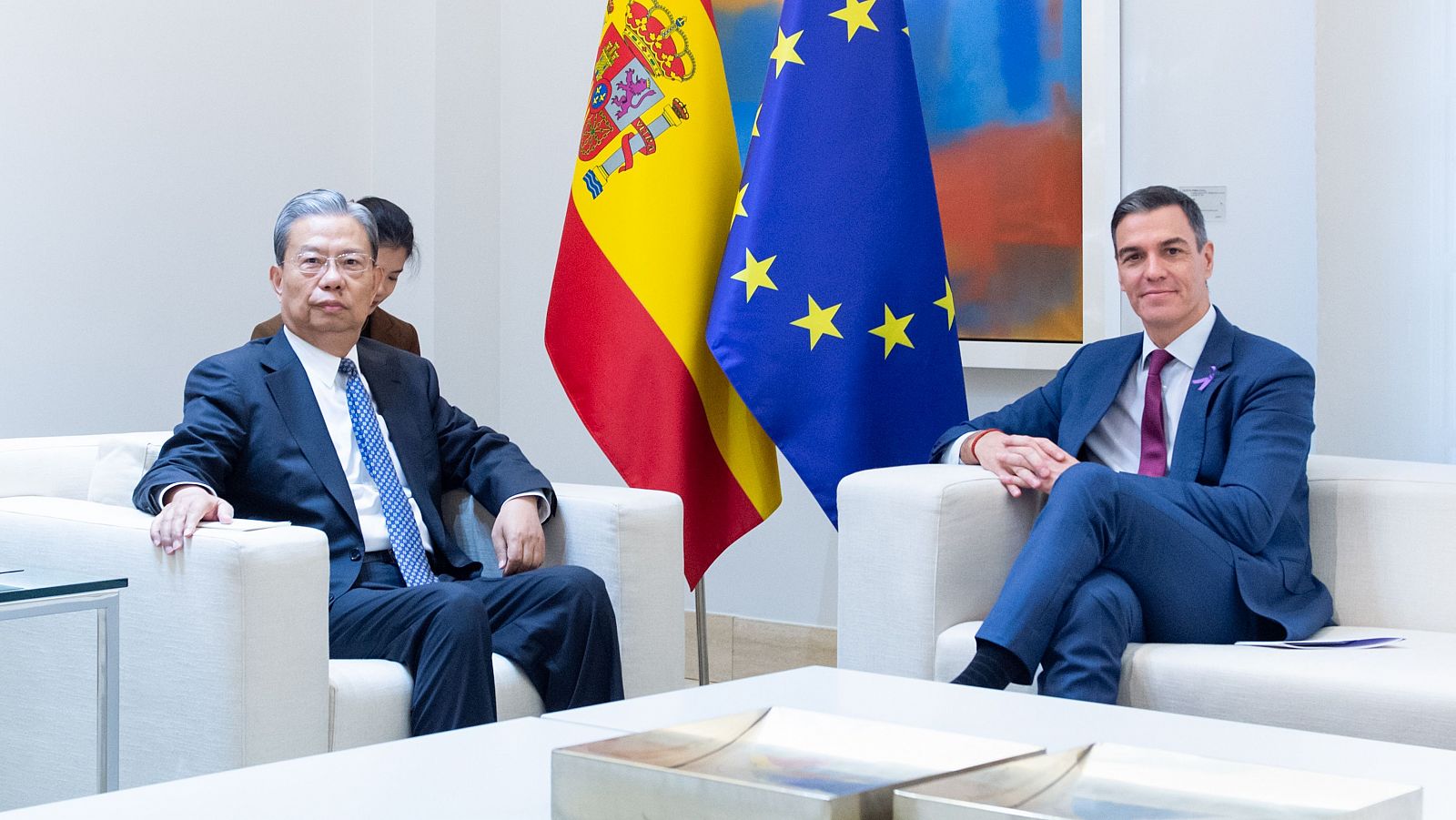 Zhao Leji y Pedro Sánchez se reúnen en La Moncloa.  Ambos llevan trajes y corbatas;  las banderas de España y la UE están presentes.