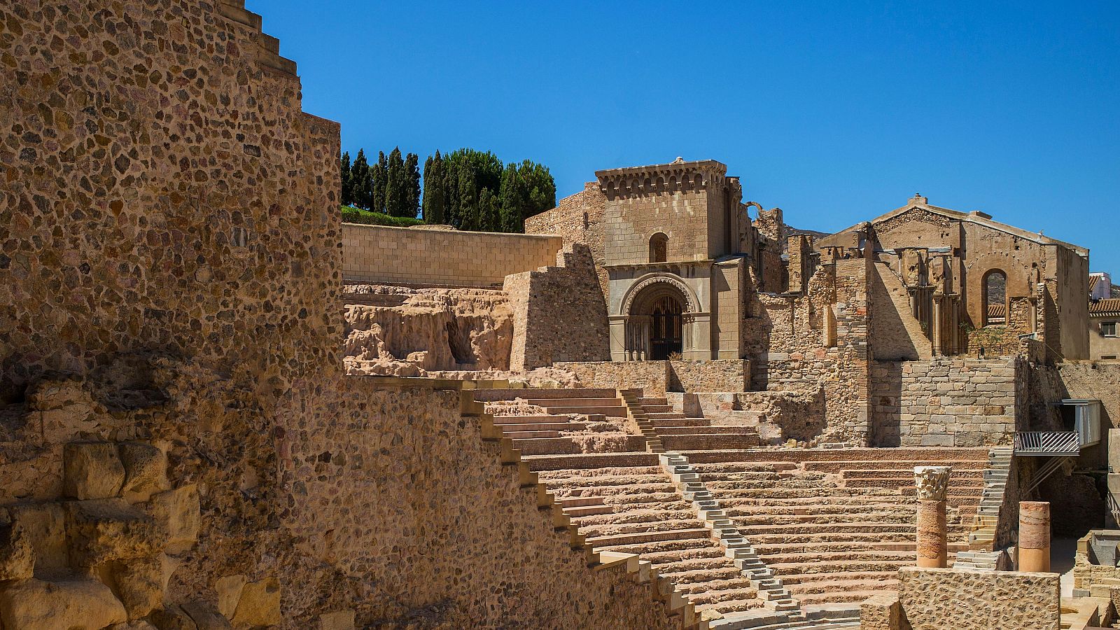 Ruinas del Teatro Romano de Cartagena: gradas, muros, columnas y arco de entrada en un día soleado.