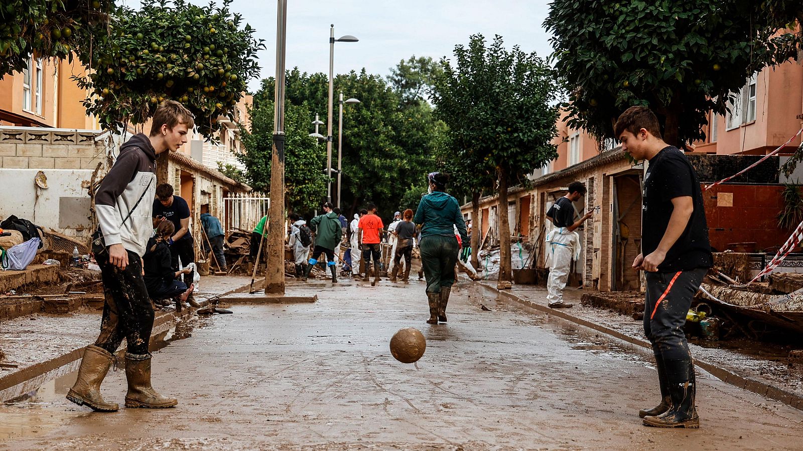 Dos jóvenes juegan al fútbol en las calles de Alfafar embarradas por la DANA.