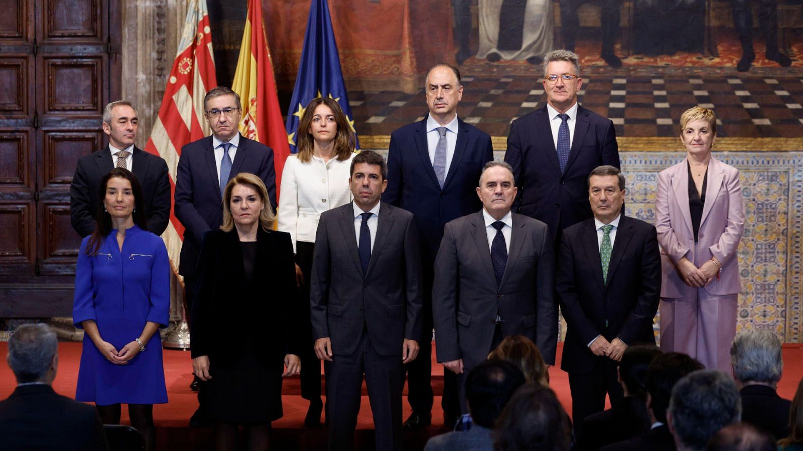 Carlos Mazón preside la toma de posesión de cuatro nuevos consejeros del Consell Valenciano.  Grupo formalmente vestido con banderas de España, Comunidad Valenciana y UE al fondo.