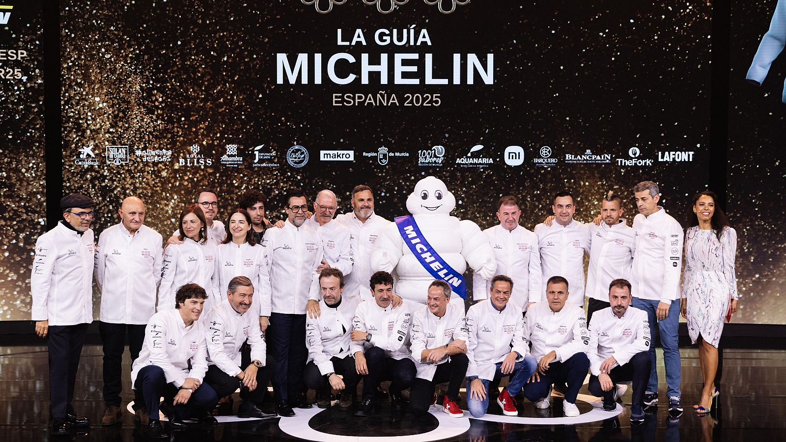 Chefs galardonados con estrellas Michelin posan junto a Bibendum en la gala de la Guía Michelin España 2025. Se ven los logos de Makro, Xiaomi y otros patrocinadores.