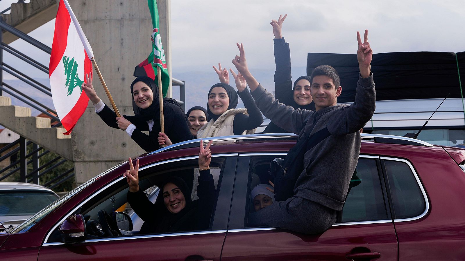 Familias libanesas celebran el alto el fuego desde un coche, ondeando banderas y haciendo gestos de paz.  El equipaje en el techo indica su regreso a casa.