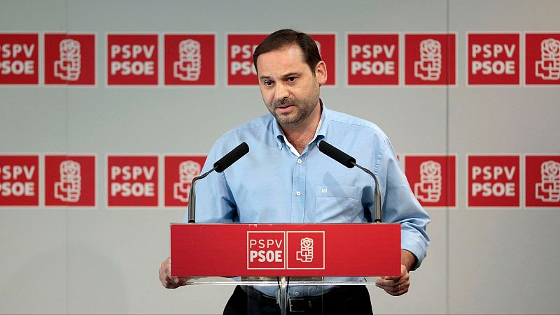 Discurso político. Persona con camisa azul clara de manga larga detrás de atril rojo con logo PSPV-PSOE. Fondo con repetición del logo.