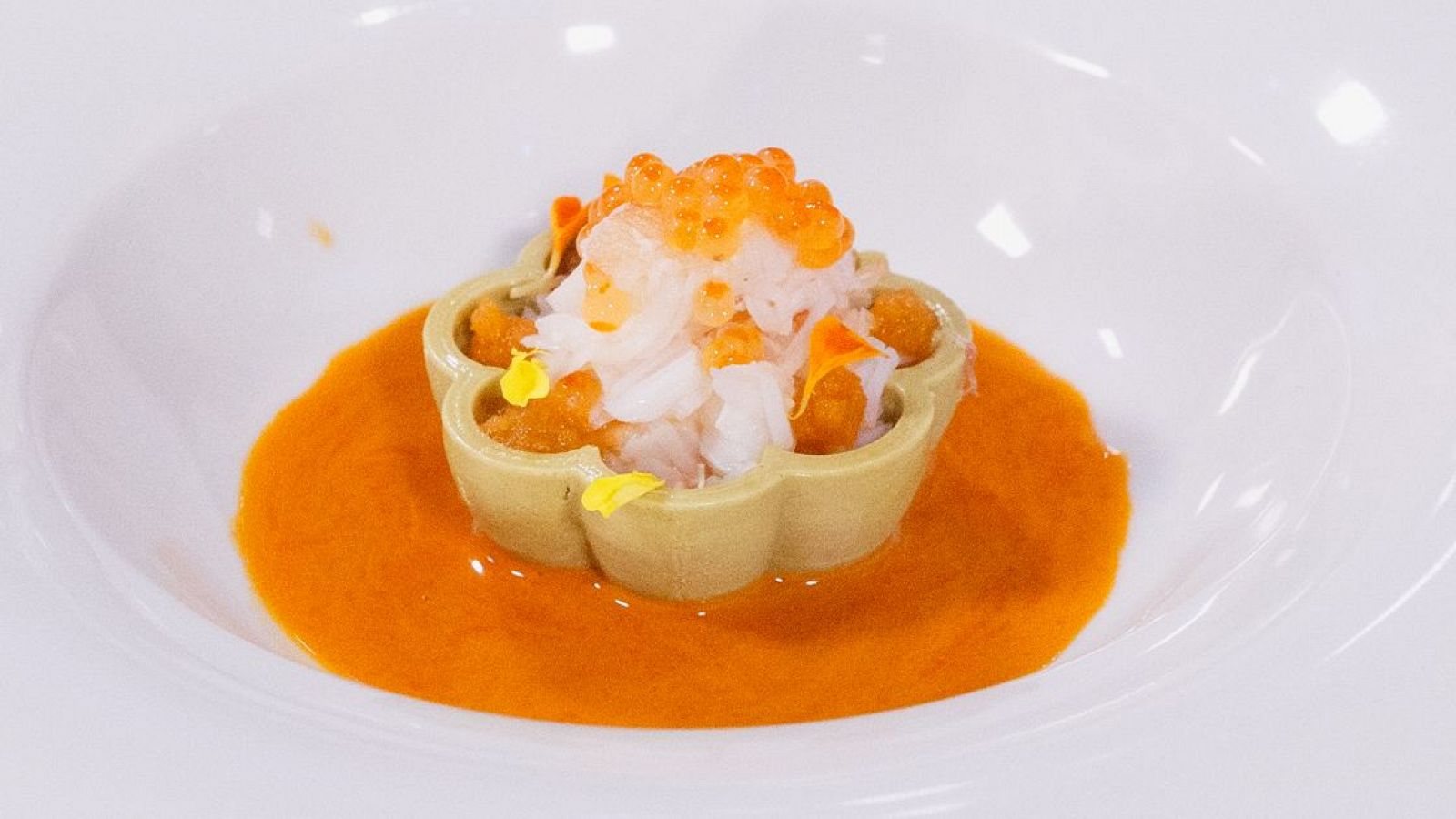 Tartaleta verde pistacho con carne de buey de mar, huevas naranjas y flores amarillas. Presentación cuidada en salsa naranja.