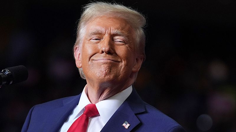 Imagen de Donald Trump en Pittsburgh, con traje azul marino, camisa blanca, corbata roja y pin de la bandera estadounidense. Sonríe ligeramente, posiblemente en un evento público.