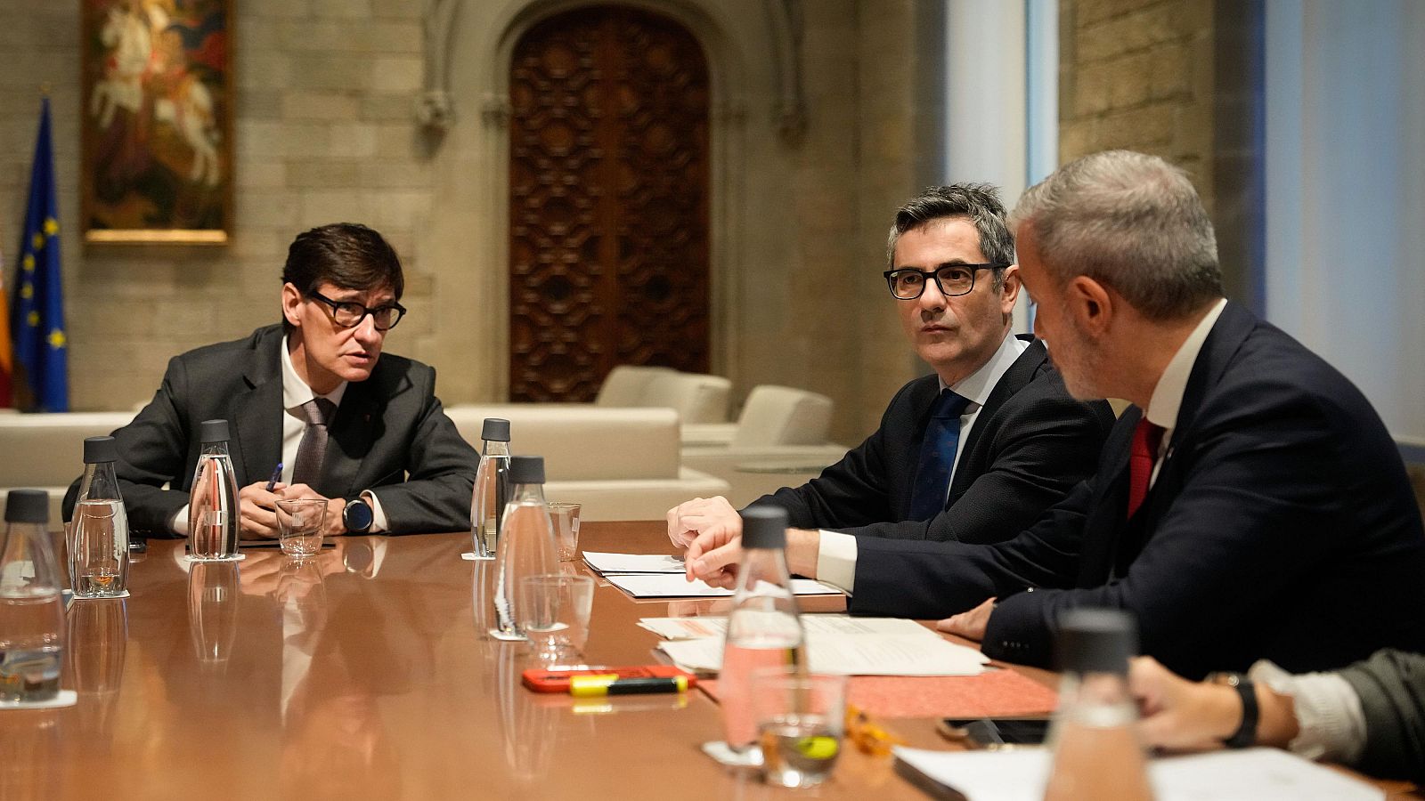 Reunión formal de tres hombres en una sala clásica.  Se aprecian trajes oscuros, documentos y una atmósfera de trabajo.