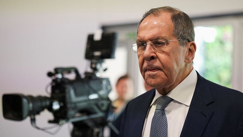 Sergei Lavrov, en traje azul oscuro y camisa blanca, con expresión seria, es filmado por una cámara de televisión durante un evento.