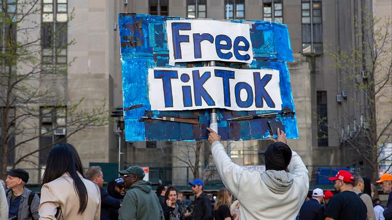 Manifestante con cartel "Free TikTok" en protesta frente a edificio gubernamental. Multitud presente, árboles sin hojas.