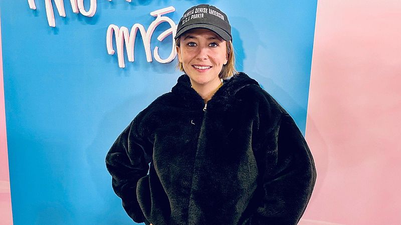 Rigoberta Bandini viste chaqueta negra y gorra con un nombre parcialmente legible en una sesión fotográfica con fondo azul y rosa.  Posible promoción de su nuevo álbum.