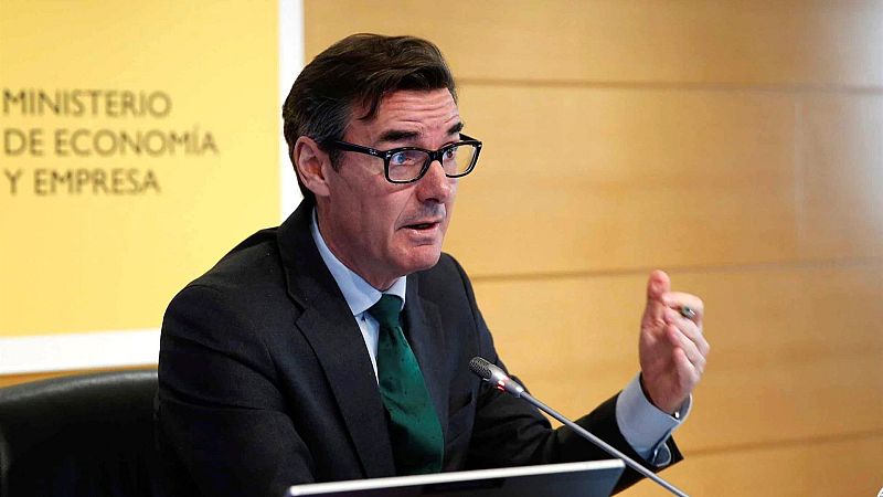 Hombre con traje oscuro y corbata verde habla ante un micrófono.  Se observa un cartel con "Ministerio de Economía y Empresa" al fondo.