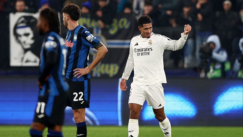 Celebración de gol de un jugador del Real Madrid, con camiseta blanca y patrocinador visible. Dos jugadores rivales, de espaldas, y parte del estadio se ven en el fondo.