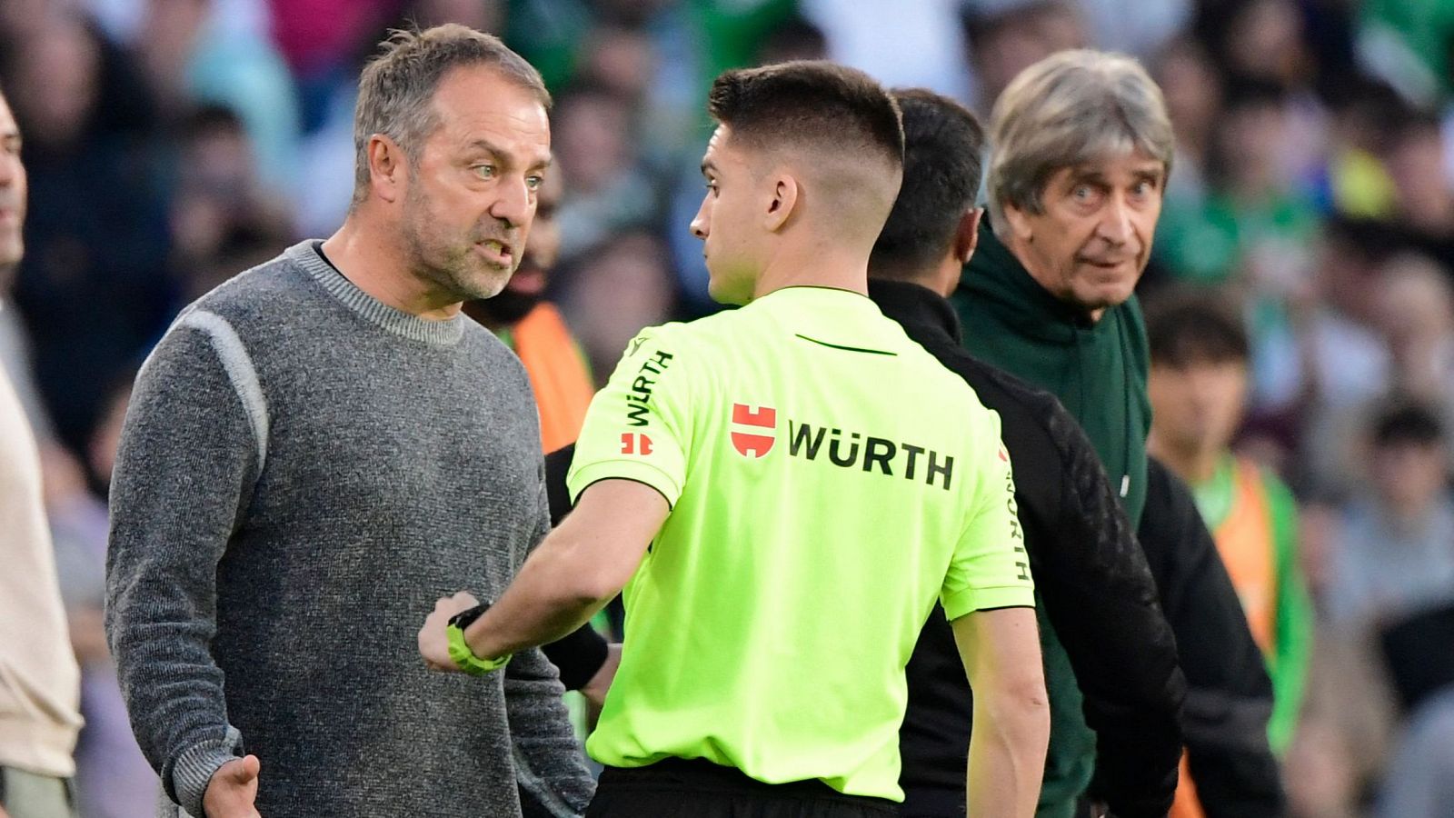 Discusión entre un entrenador y un árbitro con jersey verde fluorescente y logo Würth.  Otro hombre observa.  Contexto: partido de fútbol.