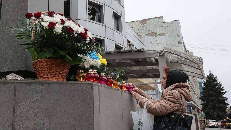 Mujer ucraniana rinde homenaje a víctimas de ataque con cohetes, colocando flores y velas junto a una clínica dañada en Zaporizhzhia.