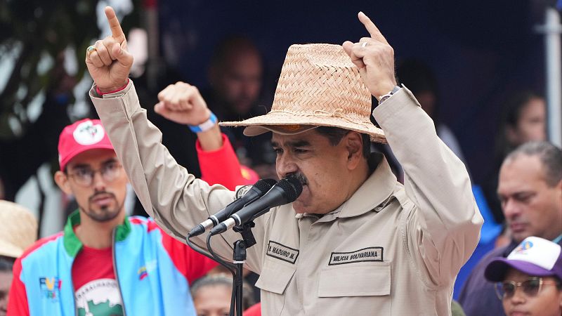 Maduro, con camisa beige y sombrero de paja, da un discurso en un acto conmemorativo.  Gestos con los dedos índices levantados mientras habla por micrófono.