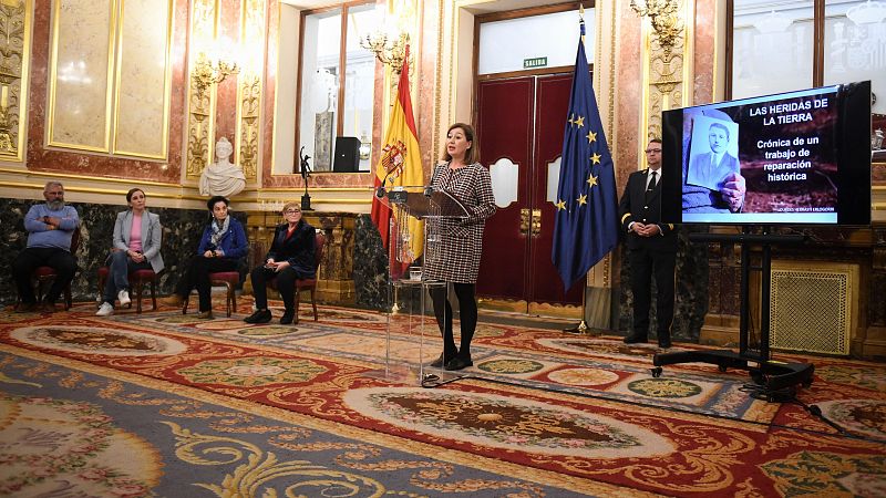 Discurso de Francina Armengol en acto formal con banderas de España y UE.  Pantalla muestra imagen en blanco y negro y texto sobre reparación histórica.