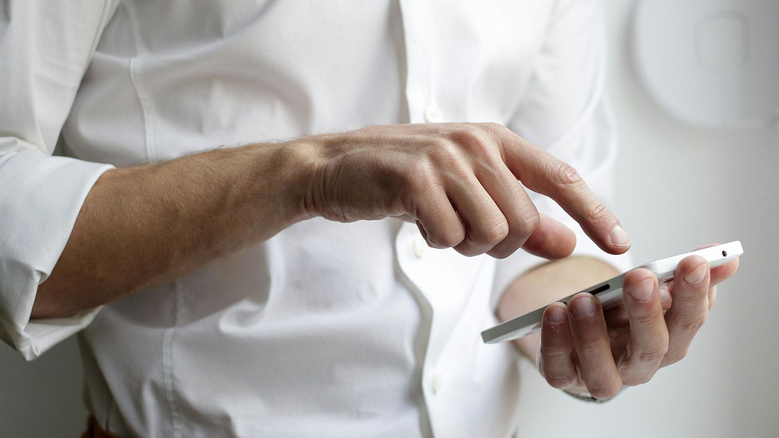 Manos usando un teléfono móvil blanco; el dedo índice interactúa con la pantalla.  El título indica un posible contexto de emergencia.