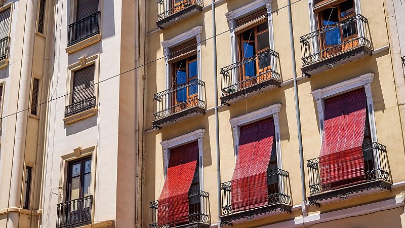 Fachada de edificio de varias plantas con ventanas y balcones, algunos con toldos rojos.  Cable eléctrico diagonal.  Posible ilustración de viviendas afectadas por regulación de alquileres.