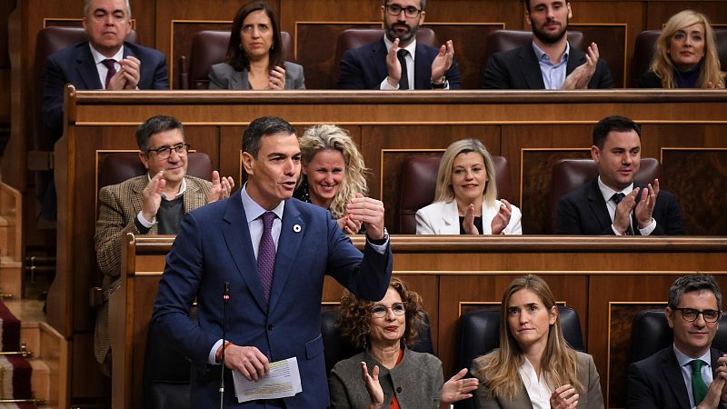 Sesión plenaria en el Congreso: Pedro Sánchez, con traje azul y corbata morada, habla y gesticula ante otros diputados.