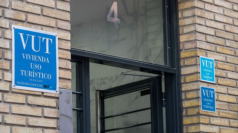 Entrada a vivienda turística en Zaragoza. Fachada de ladrillo claro, puerta gris con barrotes y carteles azules con el acrónimo VUT y número de registro.