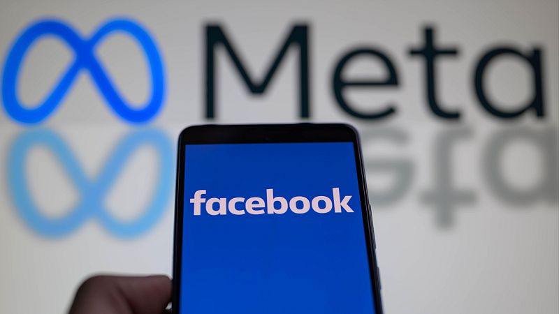 Teléfono mostrando el logo de Facebook sobre fondo azul; logo de Meta desenfocado al fondo.  Ilustración de noticia sobre multa por violación de datos.