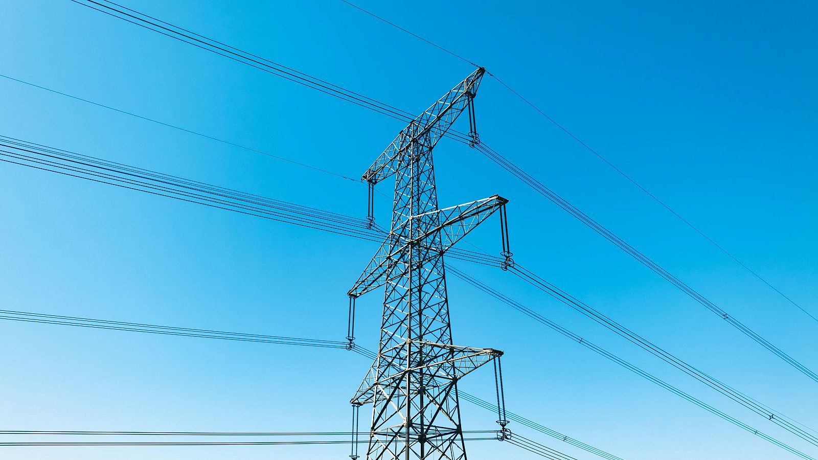 Torre de alta tensión con líneas eléctricas extendiéndose en diferentes direcciones, bajo un cielo despejado. Ilustra la infraestructura energética.