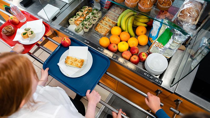 Comida de comedor escolar vista desde arriba: fruta, bollería, patatas fritas y precios en libras.  Solo el 32,5% de familias la considera de calidad.