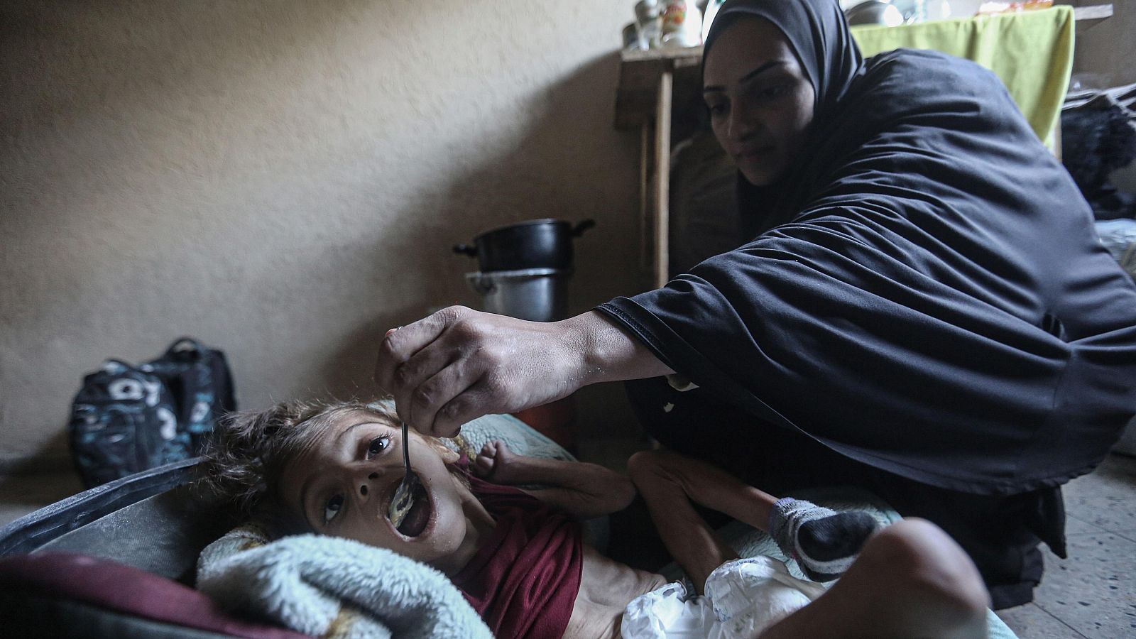 Una madre alimenta a su hija de cinco años en el campo de refugiados de Deir Al-Balah.ar agua a los gazatíes