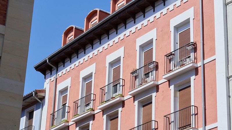 Fachada de edificio rosa salmón con balcones y persianas marrones.  Algunas plantas decoran los balcones. Ilustración sobre actualización de alquileres.