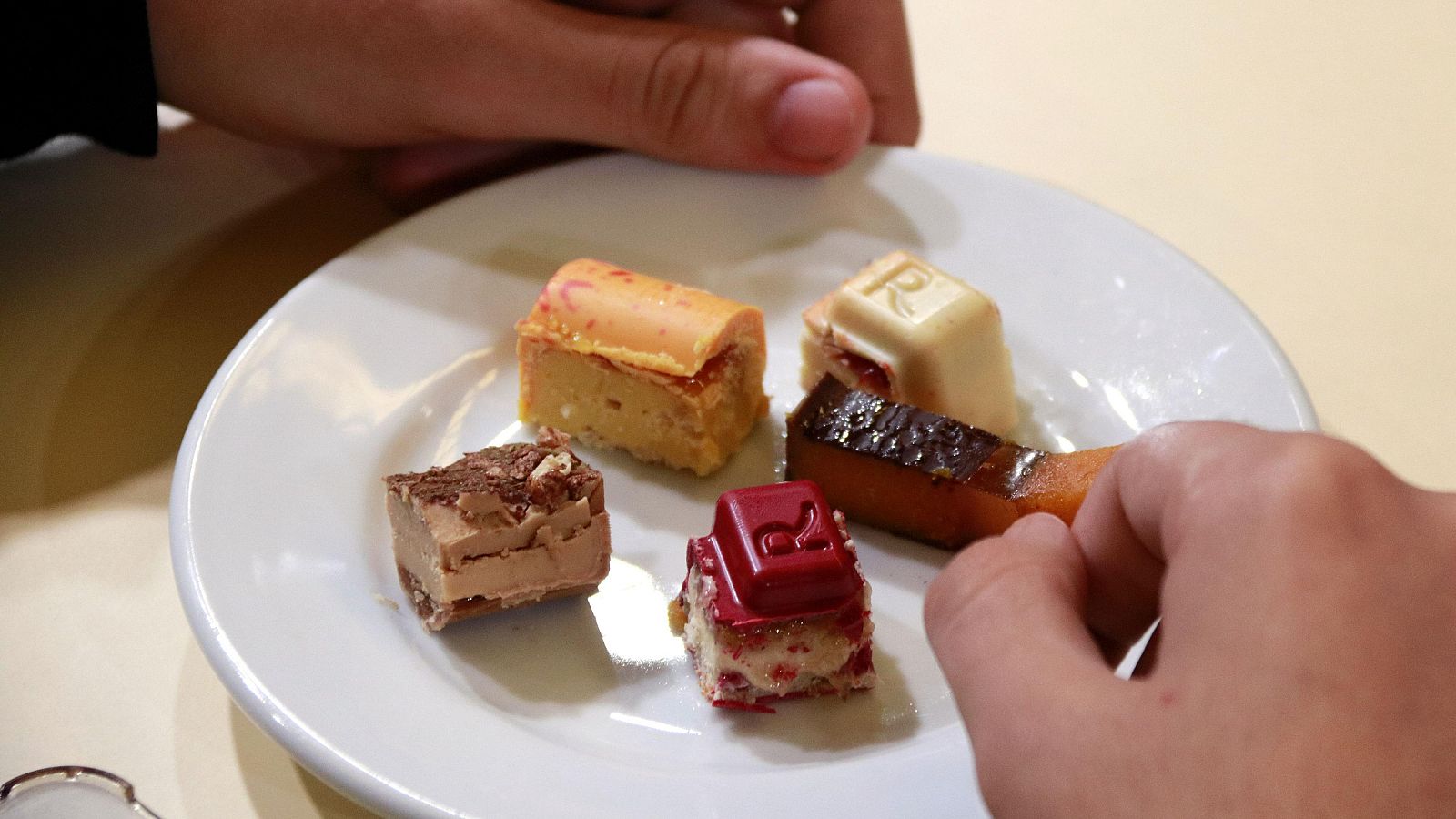 Variedad de pequeños turrones en un plato blanco. Dos manos, una ofreciendo y otra tomando un dulce. Degustación de diferentes tipos de turrón.