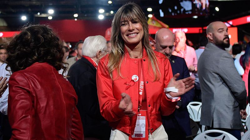Begoña Gómez, con chaqueta roja y acreditación del PSOE (pin con corazón incluido), aplaude sonriente en un acto multitudinario.